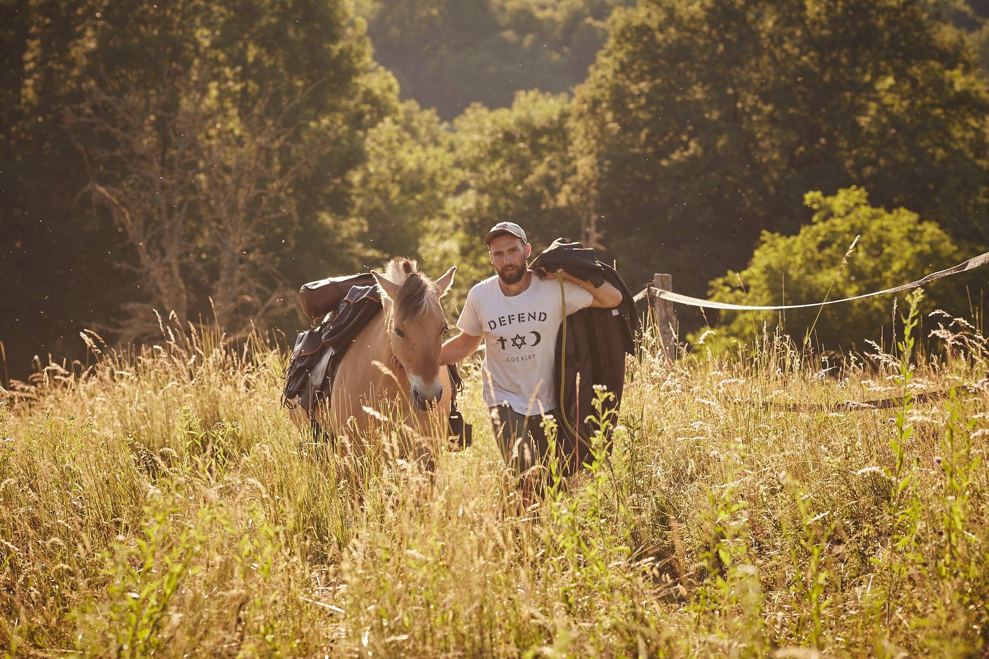 Cyril marche avec Kamaée dans les hautes herbes au soleil couchant